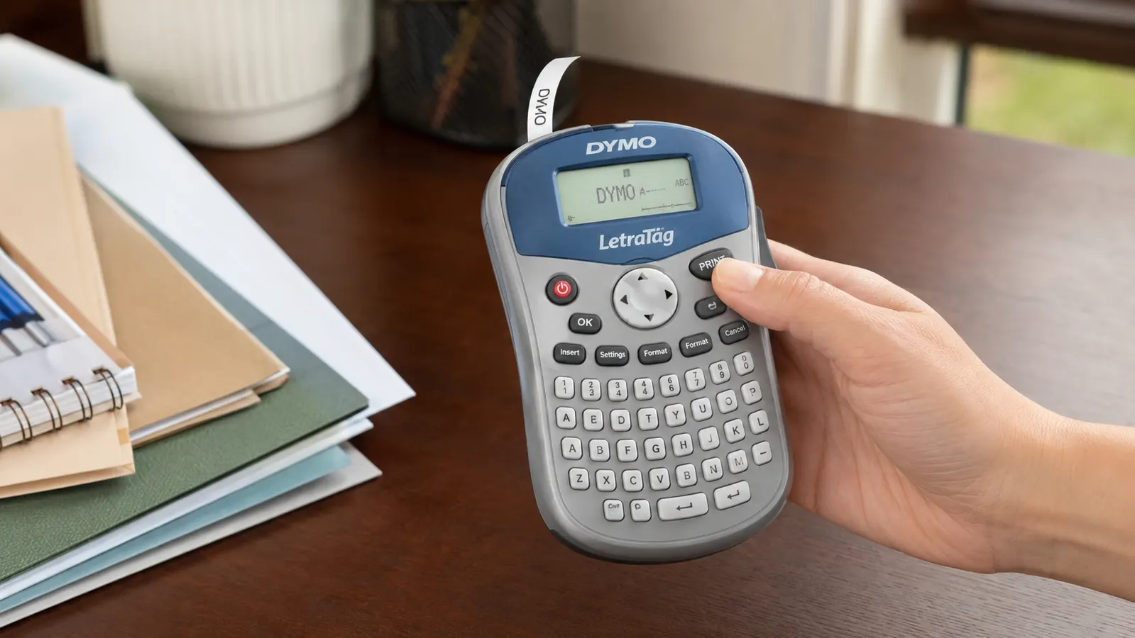 A hand printing a label with a handheld label maker at a desk