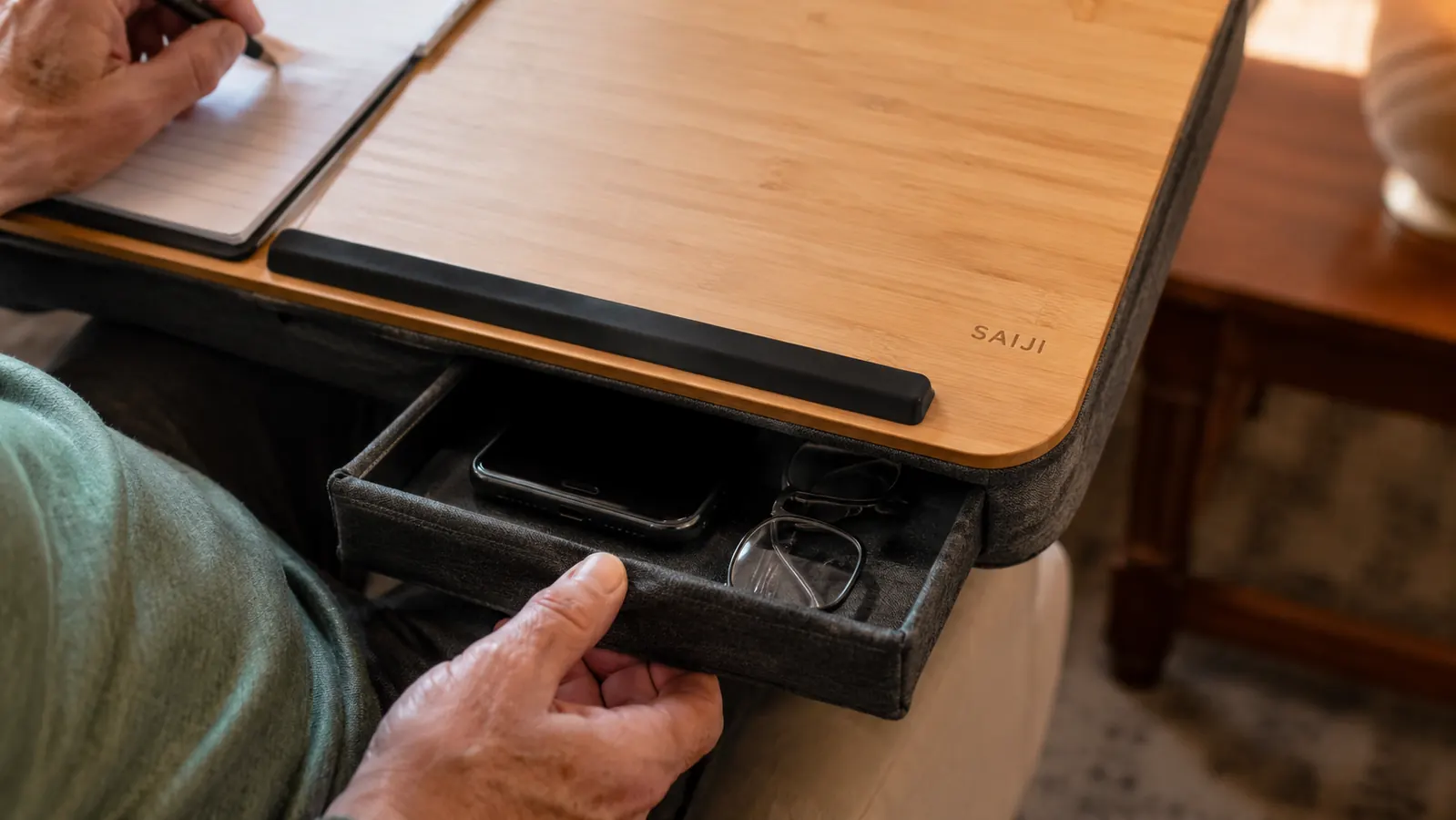 Close view of the lap desk's shallow front drawer partially open with a phone and a pair of reading glasses inside