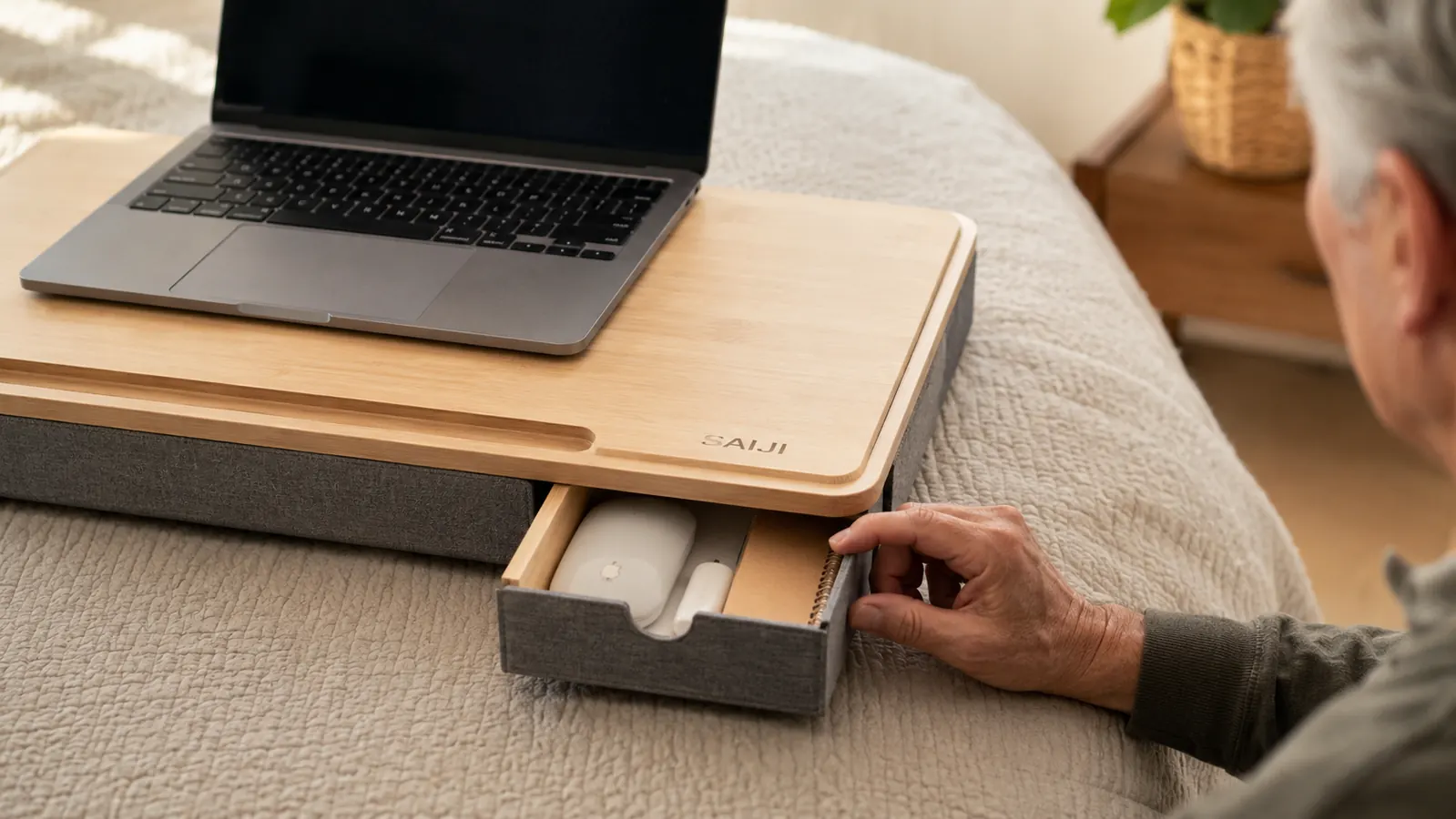 Hand pulling open the small storage drawer on a lap desk while a laptop sits on top