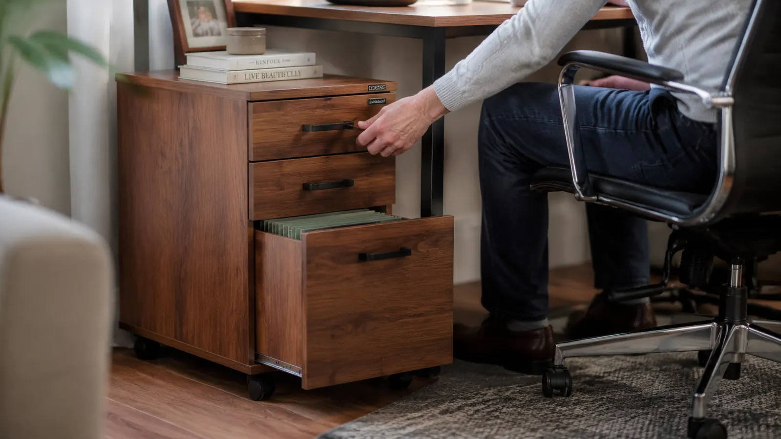 A wood rolling file cabinet with three drawers tucked under a home office desk